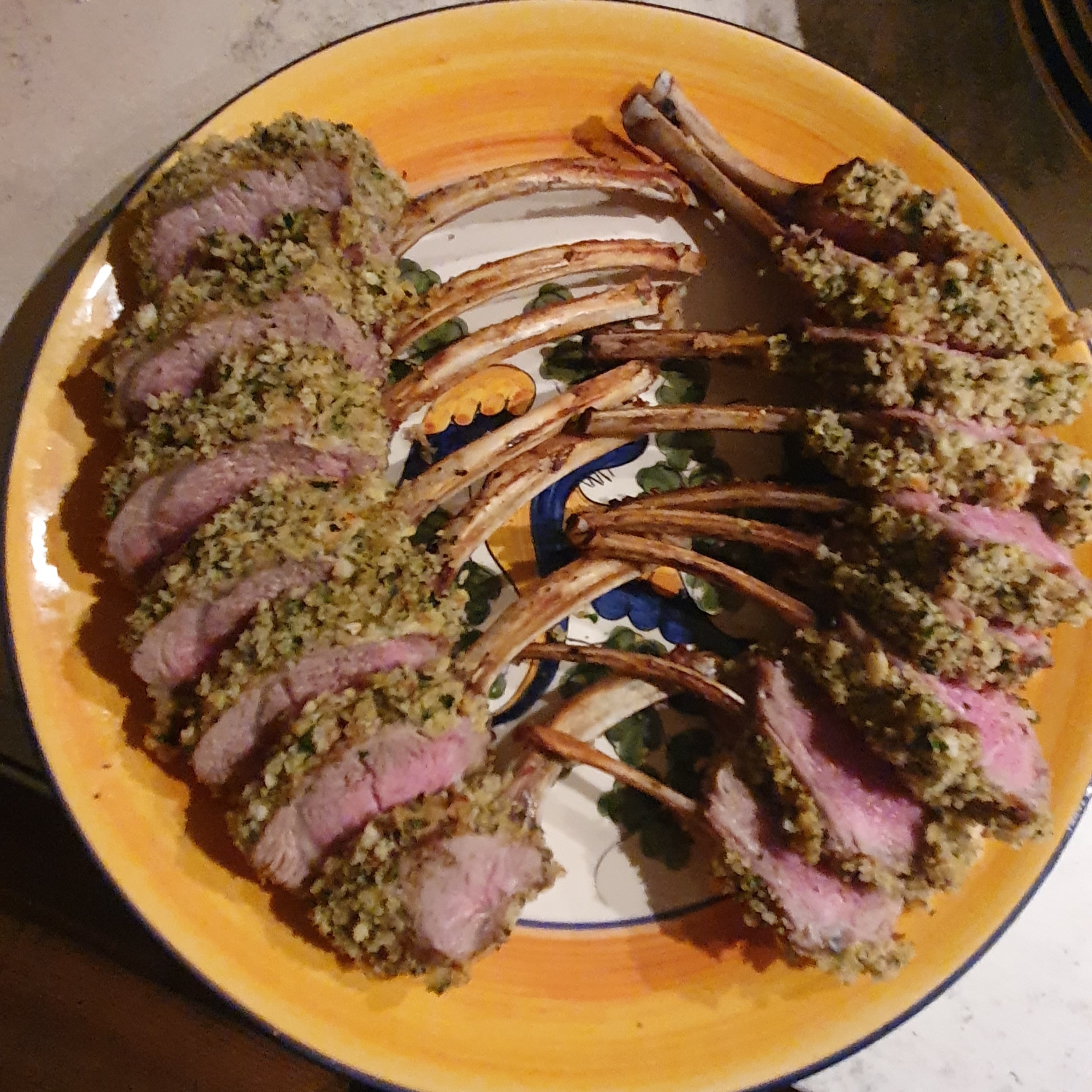 Sliced frenched rack of lamb with Provençal herb crust on a yellow ceramic platter