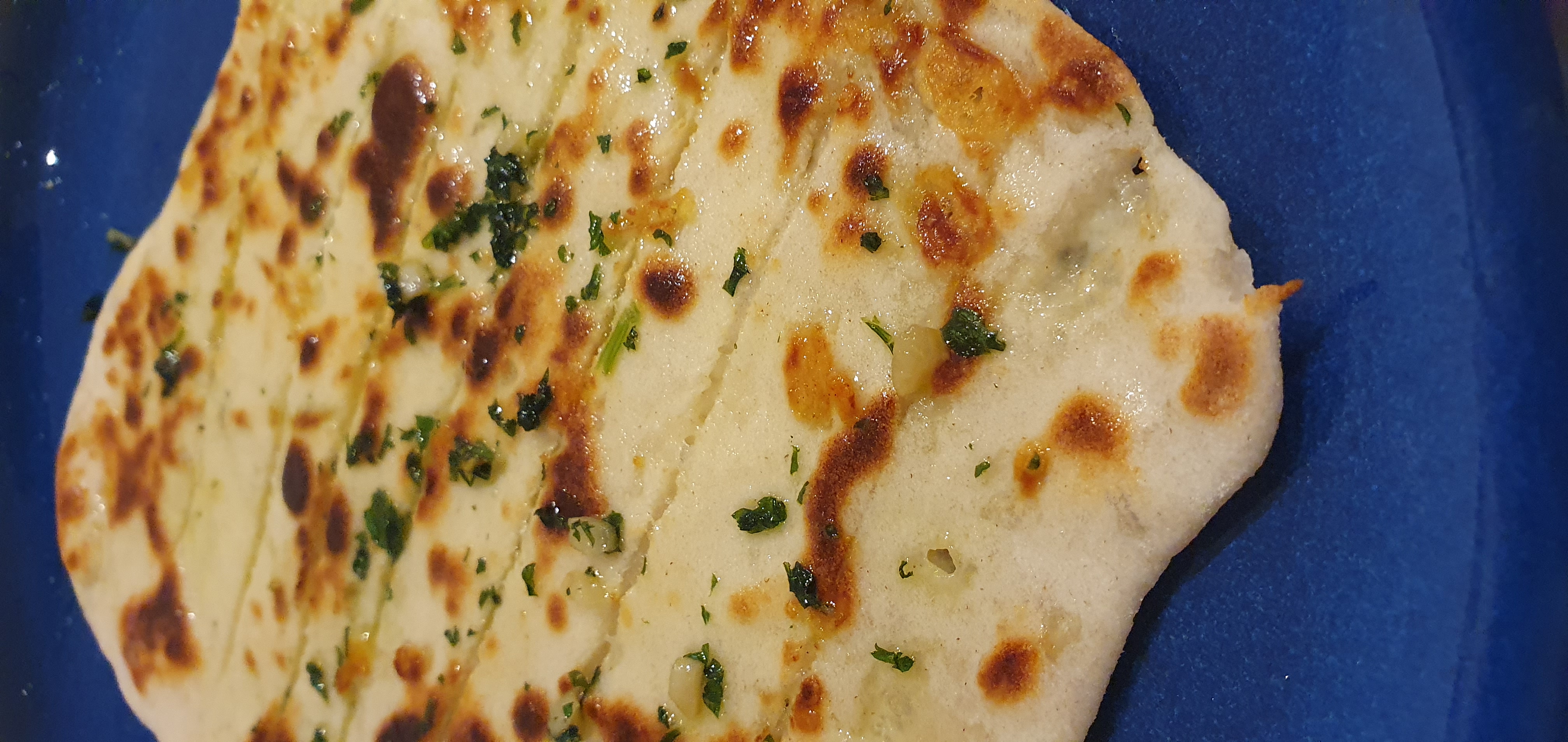 Charred Greek yogurt flatbread with garlic-parsley butter on a blue plate