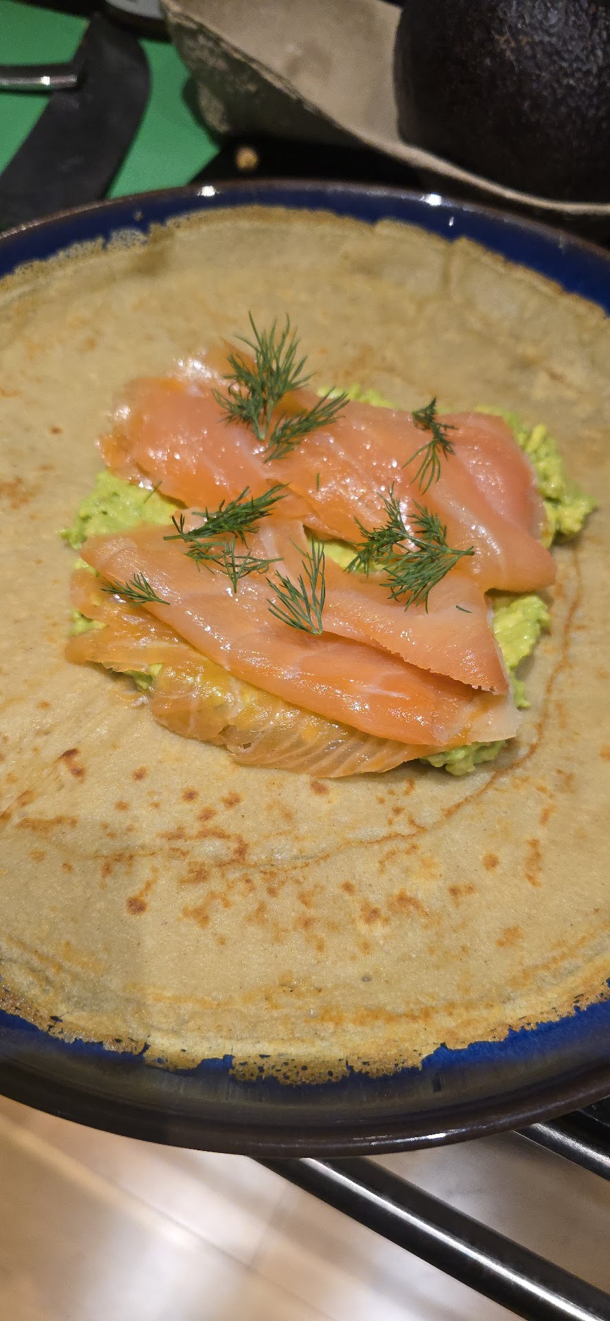 Buckwheat crepe with smoked salmon, mashed avocado and dill on a blue plate