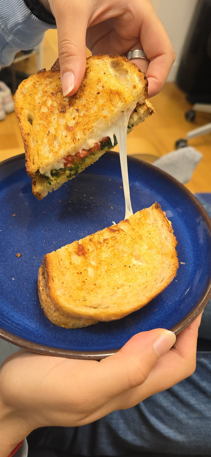 Grilled cheese sandwich pulled apart to show stretchy melted cheese, pesto and tomato over a blue plate