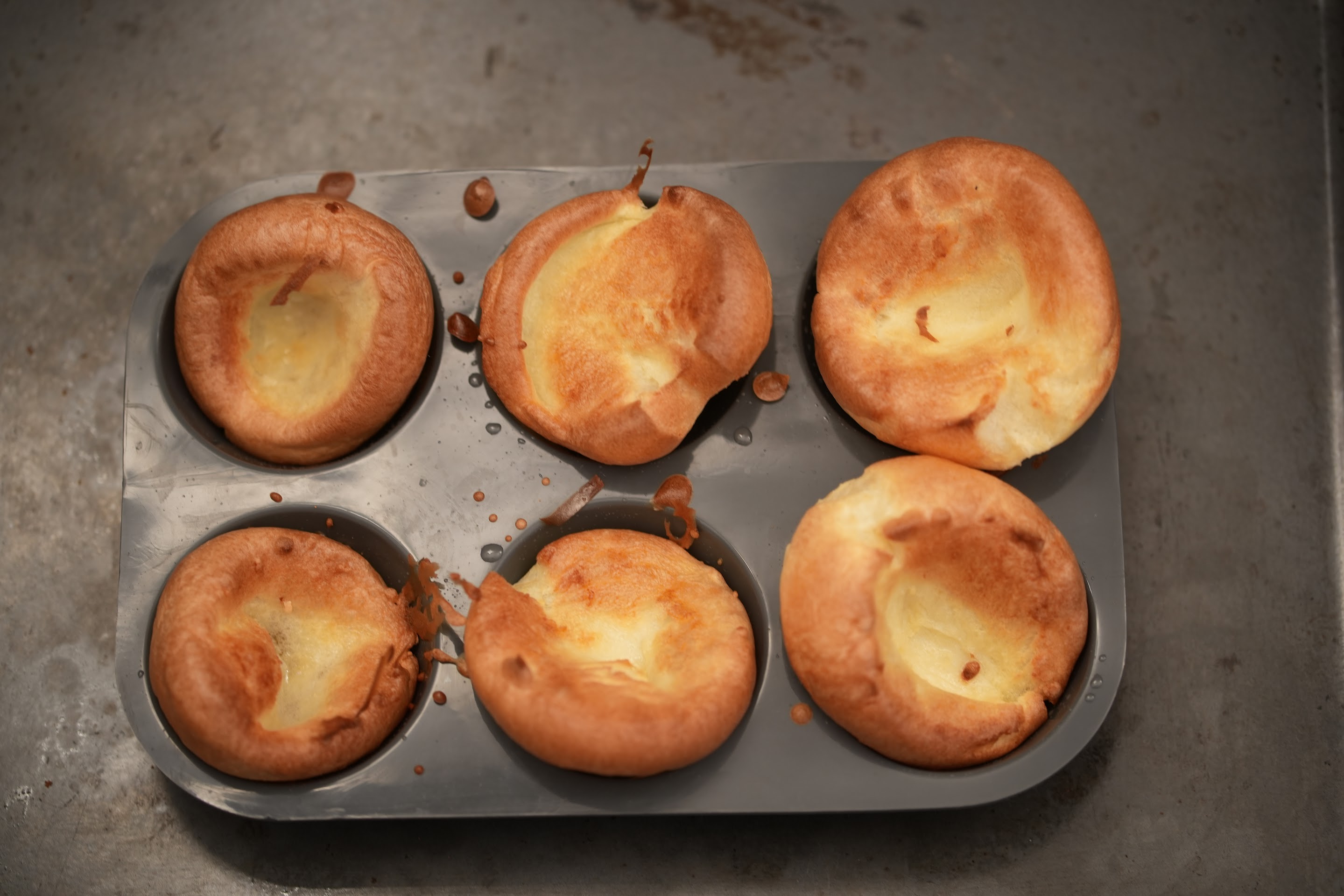 Six tall, golden Yorkshire puddings in a metal tray fresh from the oven